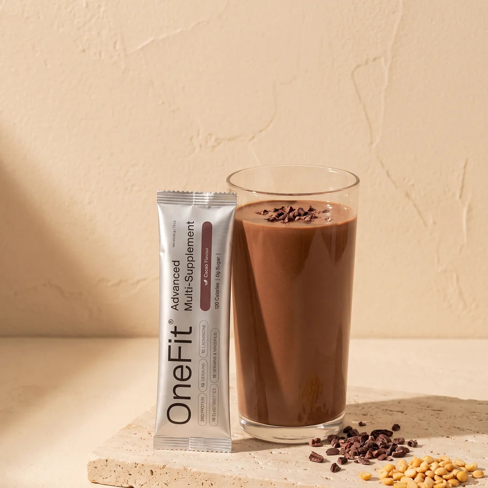 A glass of Clean Lean Protein Cacao shake beside the real sachet on a warm stone ledge with cacao nibs and yellow peas