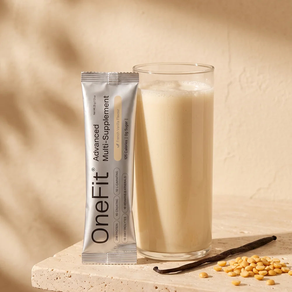 A glass of Clean Lean Protein Smooth Vanilla shake beside the real sachet on a warm stone ledge with a vanilla pod and yellow peas