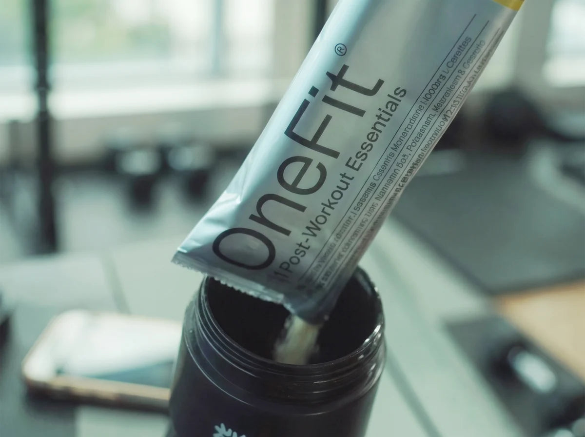 A OneFit Post-Workout Essentials sachet being tipped into a black bottle