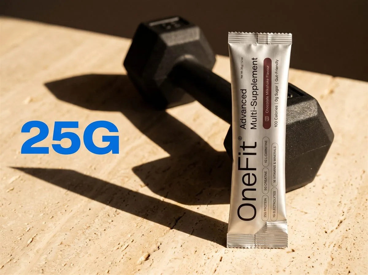 25g. A OneFit Advanced Multi-Supplement sachet standing beside a black dumbbell on warm stone in hard afternoon light