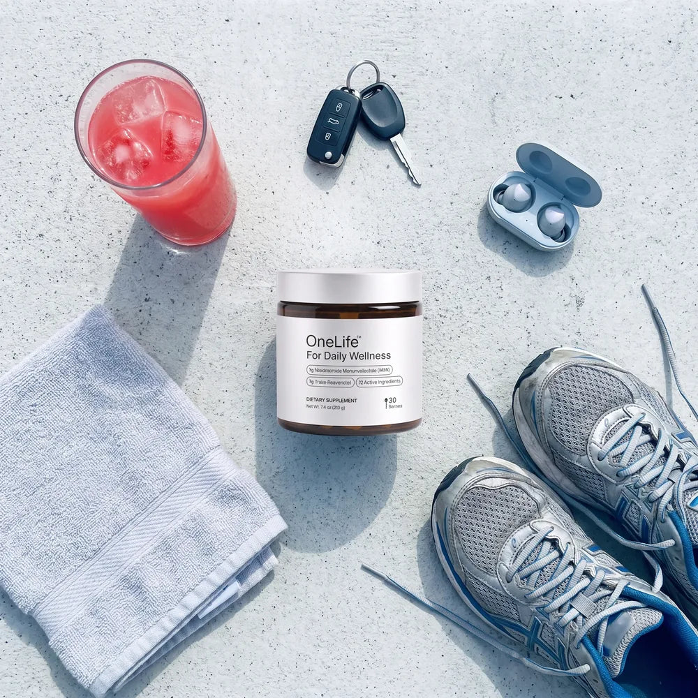 An overhead flat lay: the OneLife jar with a prepared watermelon-pink serve, keys, earbuds, a towel and running shoes