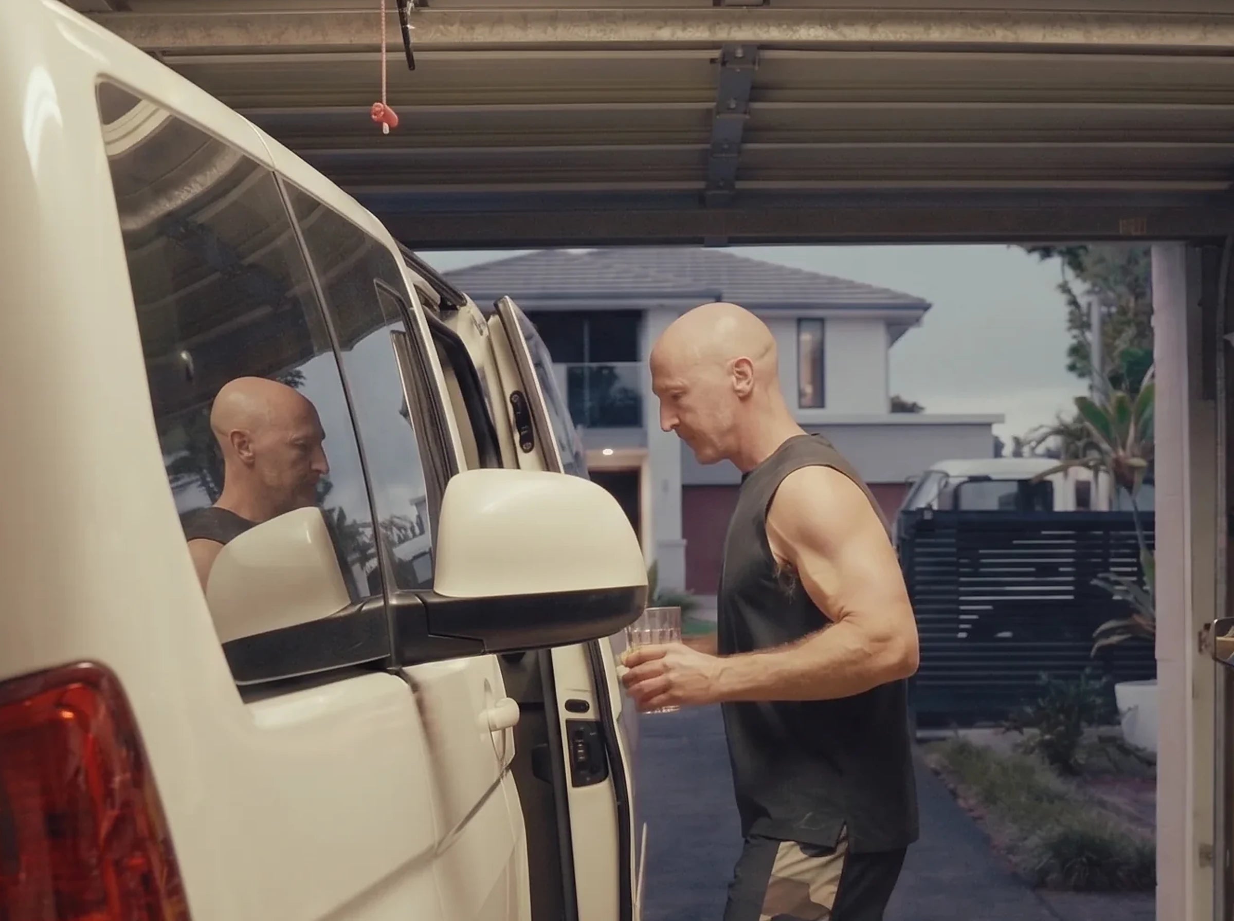 Darren walking out through his garage with his prepared OneLife serve in hand, morning light in the driveway