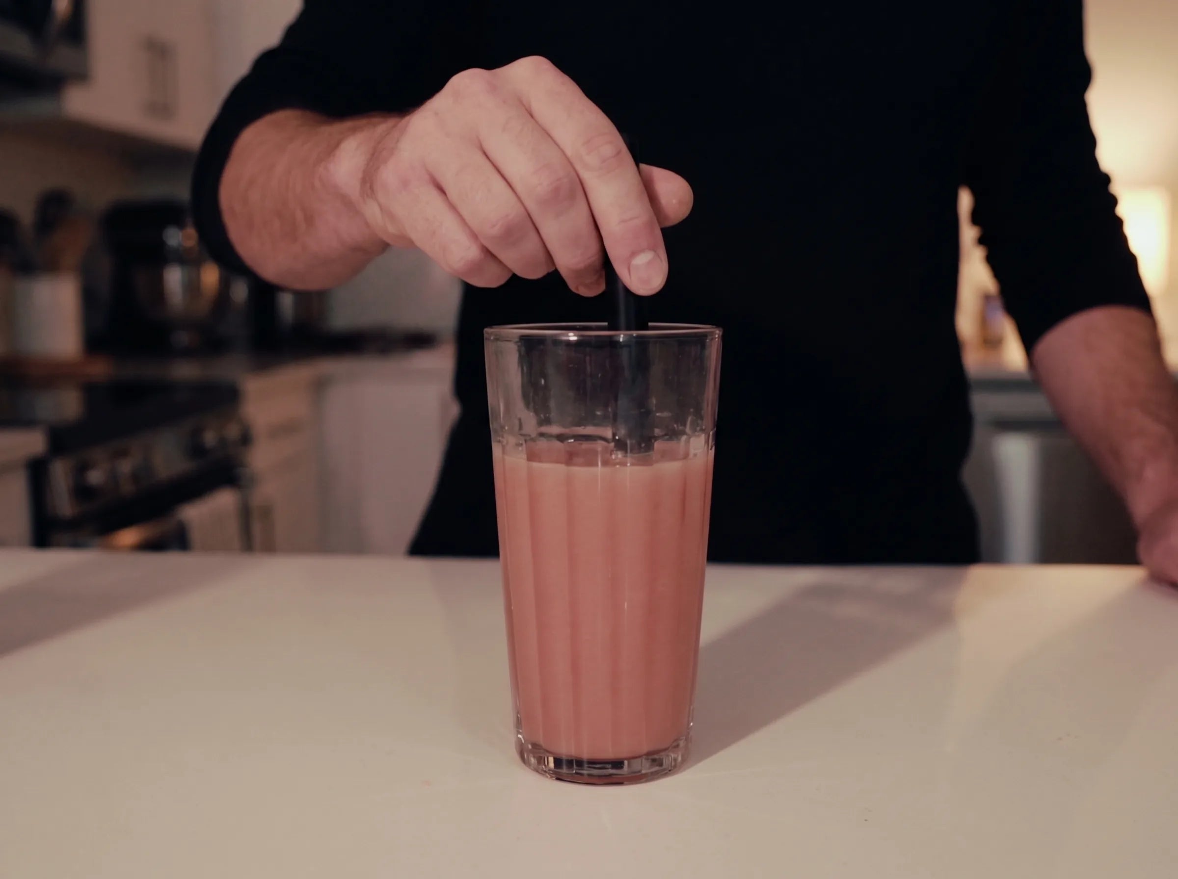 A OneLife serve being stirred at the kitchen bench, its true watermelon pink