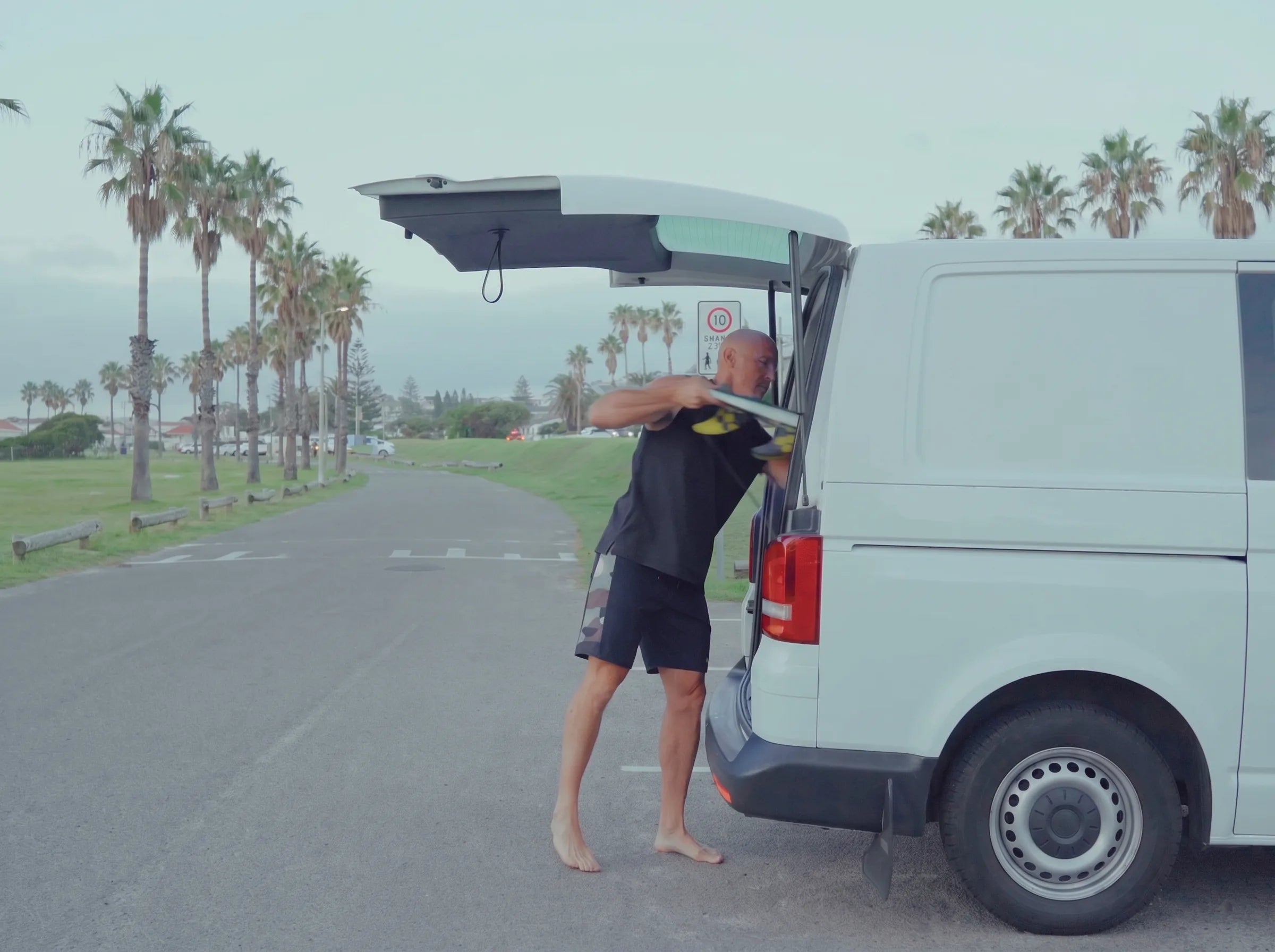 Darren sliding his surfboard into the open back of his van at the beach car park