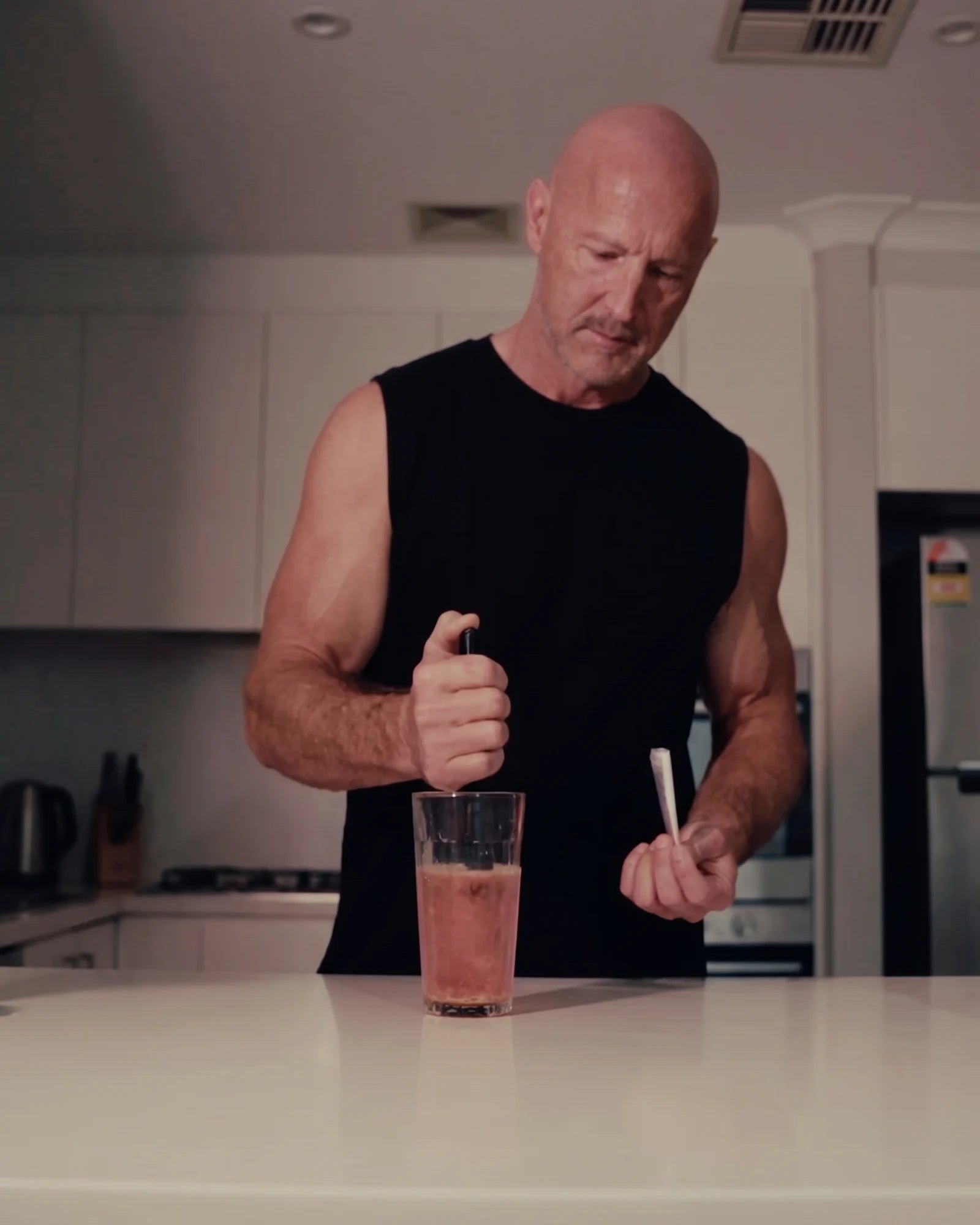 Darren stirring his measured OneLife serve at his kitchen bench, the empty sachet still in his hand