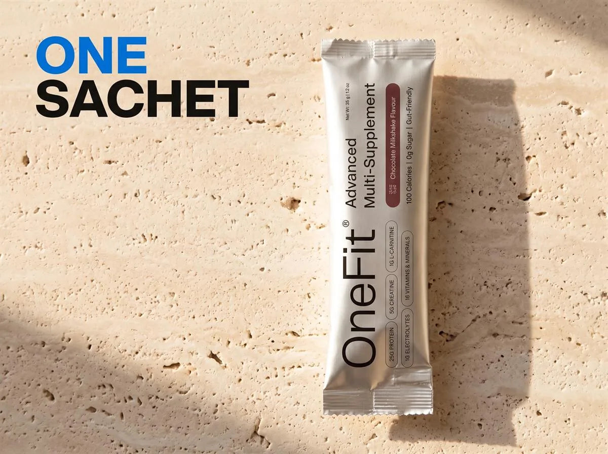 One sachet: a OneFit Advanced Multi-Supplement pack lying on warm stone, its front listing 25g protein, 5g creatine, 1g L-Carnitine, 1g electrolytes and 16 vitamins and minerals