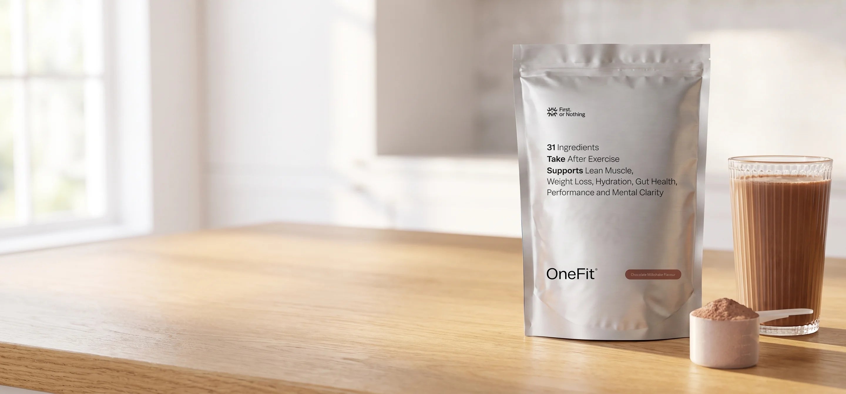The OneFit&reg; 4.7 Chocolate Milkshake pouch on a kitchen bench beside a chocolate shake and a scoop