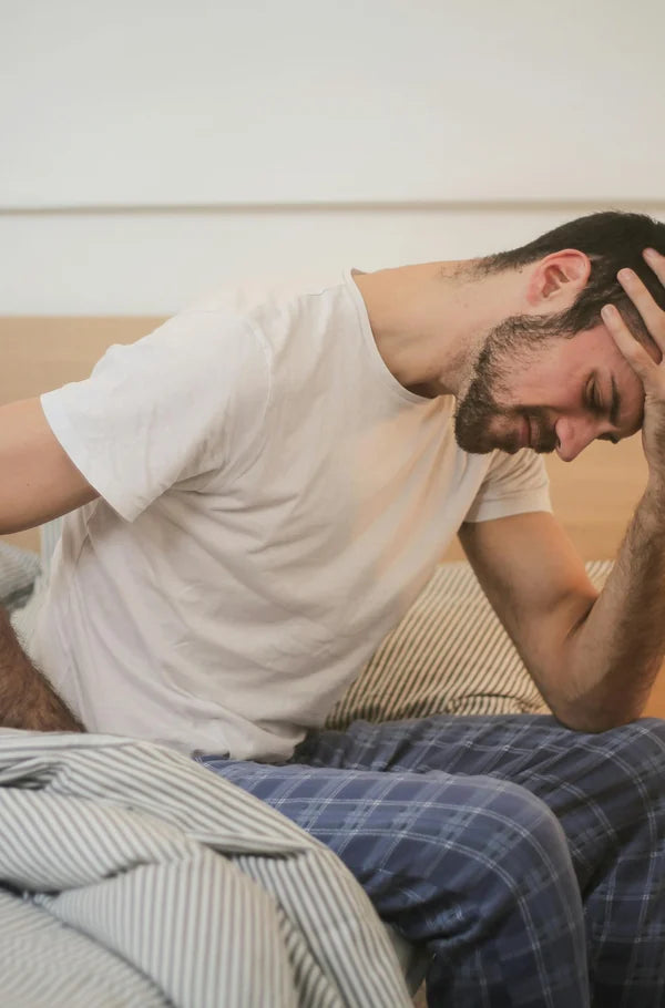 Sitting on the edge of a bed with a hand to the head